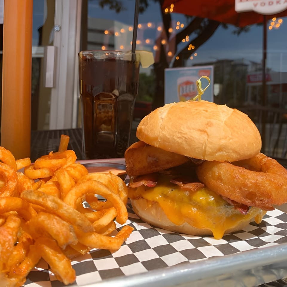 A Steyk Center burger with melted cheese, bacon, onion rings, curly fries, and a drink.